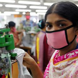 Eine Textilarbeiterin mit pinker Gesichtsmaske in Bangladesch bei der Arbeit.