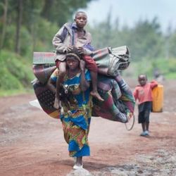 Die meisten Umweltflüchtlinge sind innerhalb ihrer Landesgrenzen als Binnenvertriebene auf der Flucht, wie hier in der Demokratischen Republik Kongo. Geflüchtete mit großen Gepäckbündeln auf dem Kopf laufen auf einer sandigen Straße im Kongo.