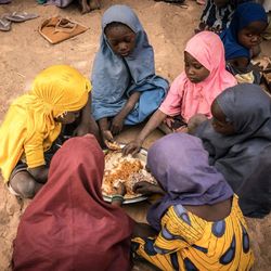 (Foto: WFP/Evelyn Fey) Sechs junge Schülerinnen sitzen um eine Schüssel mit Reis, Gemüse und Bohnen, die sie sich teilen.