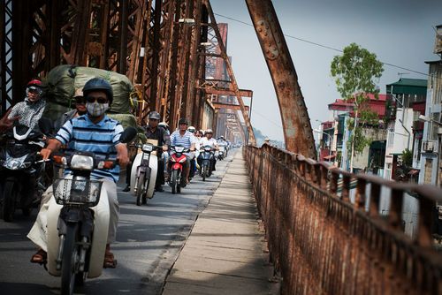 Viele Mopedfahrer fahren in einer Reihe über eine rostige Brücke.