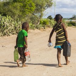 Der Süden Madagaskars ist häufig von verschiedenen Klimawandelfolgen wie Dürre betroffen. Zwei Kinder laufen über eine staubige Straße und tragen leere Wasserkanister.