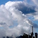 Schornsteine einer Fabrikanlage stoßen dunkle Abgaswolken aus