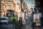 Aktivisten stehen mit Mundschutz und Gasmasken auf der Straße und halten Schilder mit der Aufschrift "Toxic Airzone" vor sich