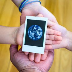Vier Hände halten ein Polaroid-Foto der Erde.