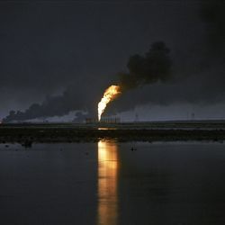 Vor einem dunklen, nächtlichen Himmel sieht man viel Rauch und Flammen, die aus einer Ölraffinerie kommen.