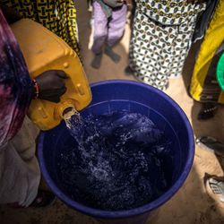 Eine Tonne wird mit Wasser aufgefüllt während viele Menschen und um ihn herum stehen und nach ihm greifen