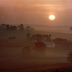Morgensonne über Pennsylvania Dutch County, USA Morgennebel bedenkt eine Landschaft, die aufgehende Sonne färbt alles rötlich.