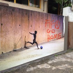 Auf einer Mauer in Sao Paulo ist ein fußballspielender Junge abgebildet, neben ihm stehen die Worte "Fifa go home" als Zeichen des Protests gegen die Ausbeutung durch den Fußballverband. 