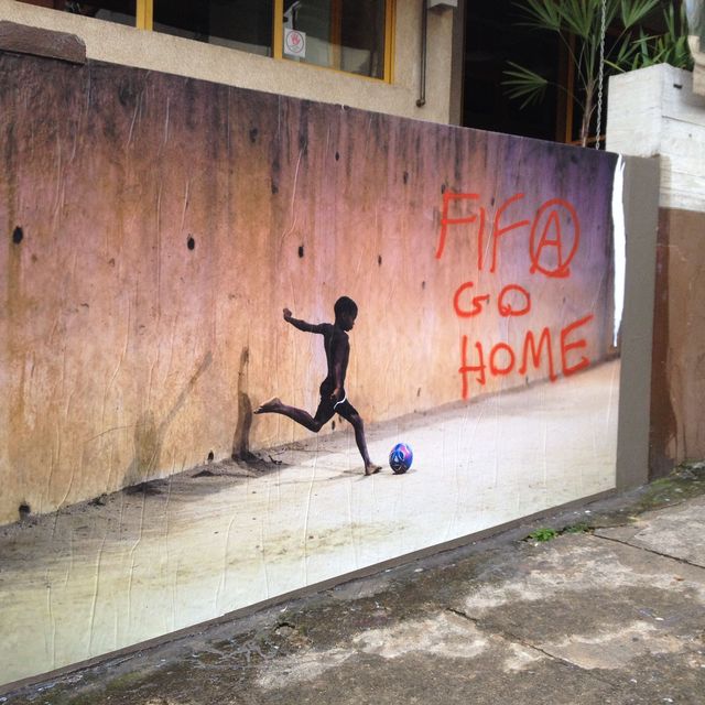 Auf einer Mauer in Sao Paulo ist ein fußballspielender Junge abgebildet, neben ihm stehen die Worte "Fifa go home" als Zeichen des Protests gegen die Ausbeutung durch den Fußballverband.