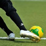 Bildausschnitt eines Beines mit Stollenschuh, der einen Fußball tritt.
