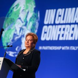 Eine Frau steht an einem Redepult mit Mikrofon. Im Hintergrund sieht man das Logo der COP26