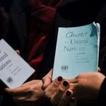 Eine Hand hält eine abgegriffene Ausgabe der UN Charta, im Hintergrund ist eine weitere Ausgabe zu sehen.